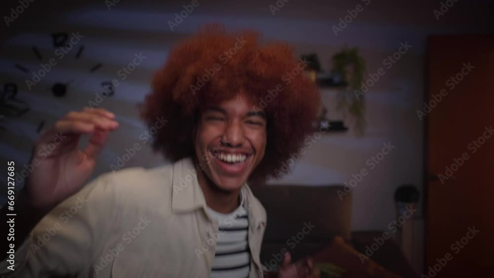 Close up handsome young afro man has fun dancing alone in living room at night. Excited Latin male influencer doing viral dance moves for social media. Generation z people enjoying free time at home. Close up handsome young afro man has fun dancing alone in living room at night. Excited Latin male influencer doing viral dance moves for social media. Generation z people enjoying free time at home.