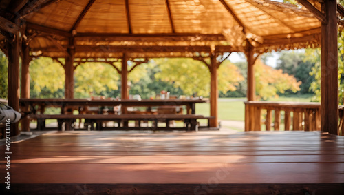 A wooden gazebo with a thatched roof in a park. The gazebo has a wooden table and benches. In the background is a blurred view of the park with trees and grass