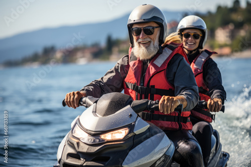 Happy senior Caucasian couple in safety helmets and vests riding jet ski on a lake or along sea coast. Active elderly people having fun on water scooter. Healthy lifestyle for retired persons.