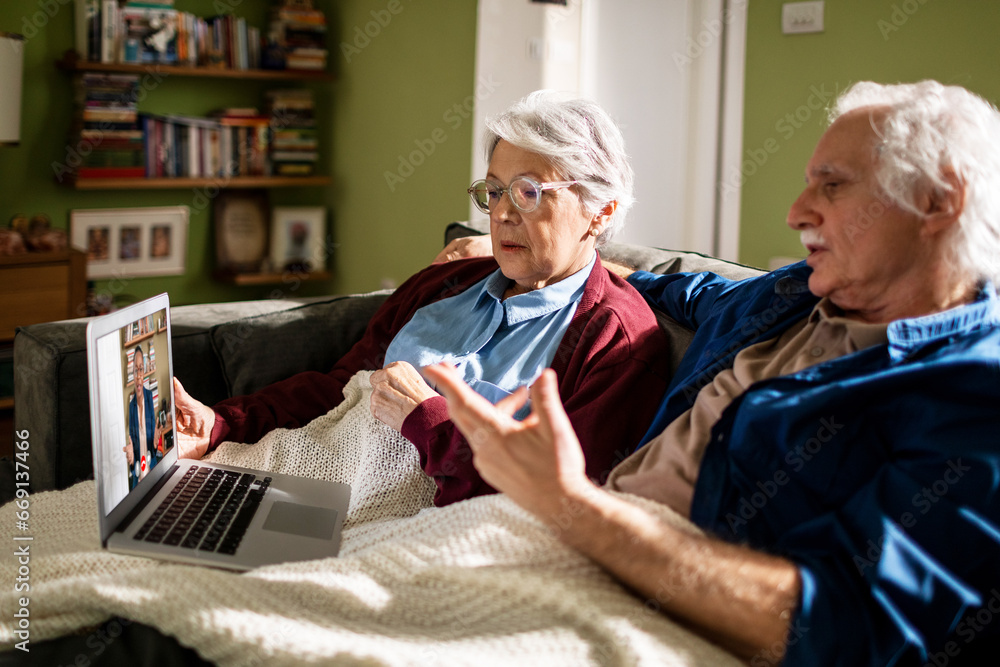 Senior couple engaged in a video call from their living room Senior couple engaged in a video call from their living room