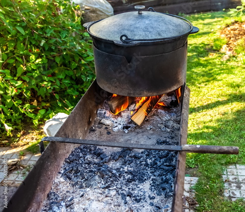 Metal cauldron with lid on the fire of the grill close-up on the background of greenery in summer