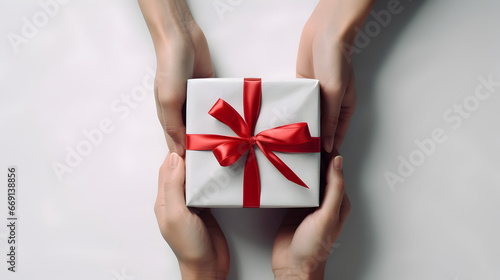 Hands giving and receiving christmas gift box on a white background. Luxury wrapped present with red color ribbon and bow. Isolated, aesthetic and minimalist.