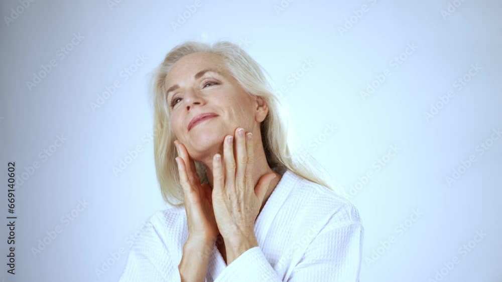 Mature smiling woman wearing robe touching face, spa concept of beauty, looking and smiling at camera, white background Mature smiling woman wearing robe touching face, spa concept of beauty, looking and smiling at camera, white background