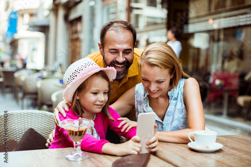Young family using the smartphone together in a outdoor cafe sitting area in the city