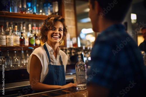 A friendly, smiling female bartender converses with a customer behind the bar counter photo