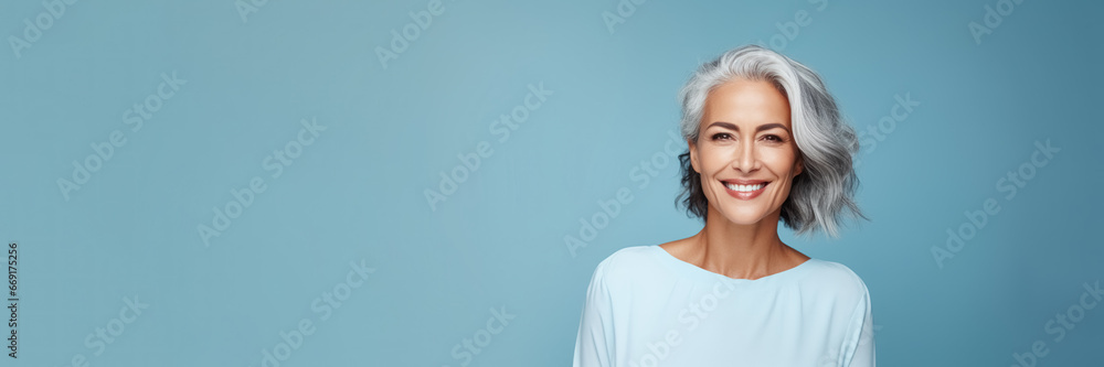 Adult woman, graced with silvery hair, healthy skin and warmth smile on blue banner background with copy space. Concept skin care, beautiful and glowing aging Adult woman, graced with silvery hair, healthy skin and warmth smile on blue banner background with copy space. Concept skin care, beautiful and glowing aging