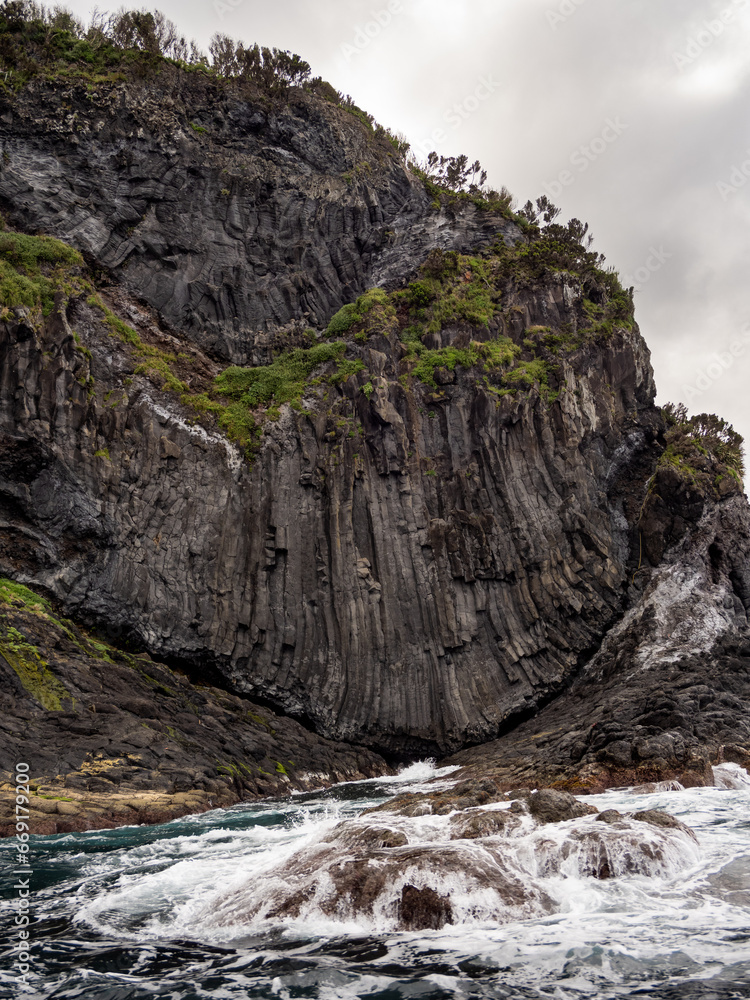 Obraz premium Water from the Atlantic Ocean reaching the jagged coast, with prismatic shapes, of Flores Island.
