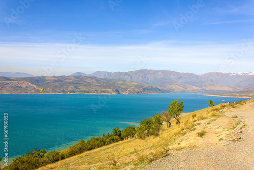 View of the Charvak reservoir from the shore. Autumn landscape of Uzbekistan: a bright blue lake and yellowed grass.