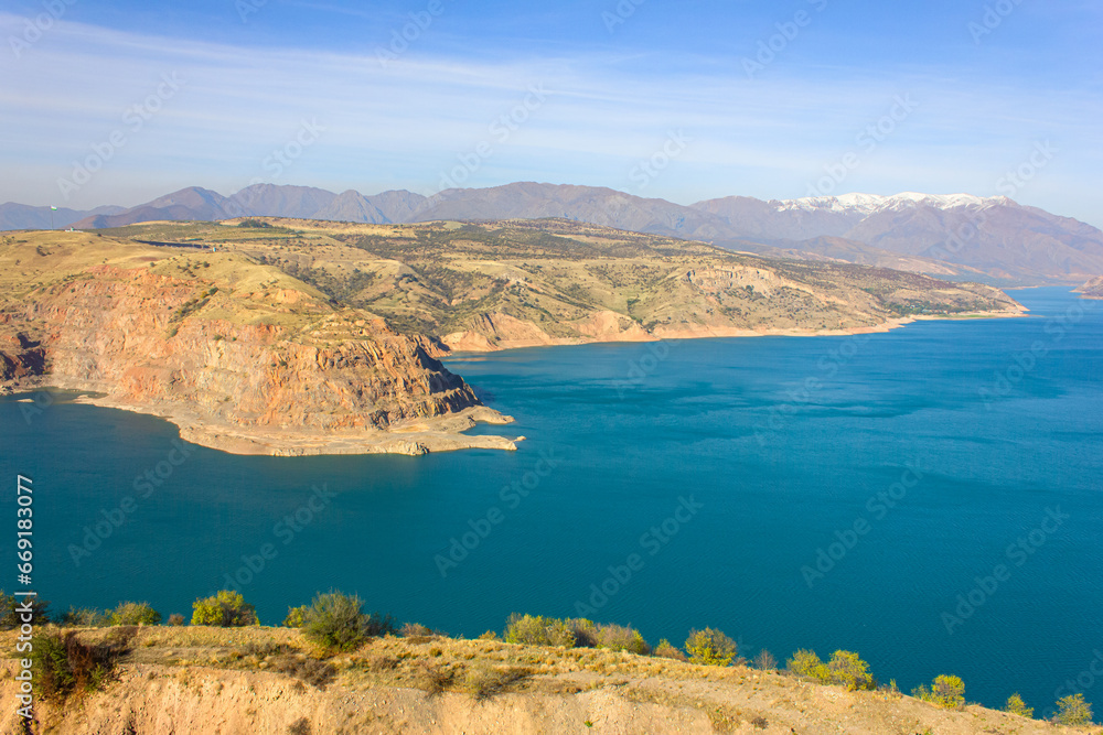 View of the Charvak reservoir from the shore. Autumn landscape of Uzbekistan: a bright blue lake and yellowed grass.