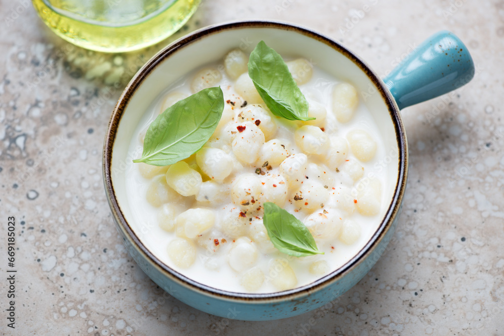 Turquoise serving bowl with potato gnocchi in cheese sauce, horizontal shot on a beige granite background Turquoise serving bowl with potato gnocchi in cheese sauce, horizontal shot on a beige granite background