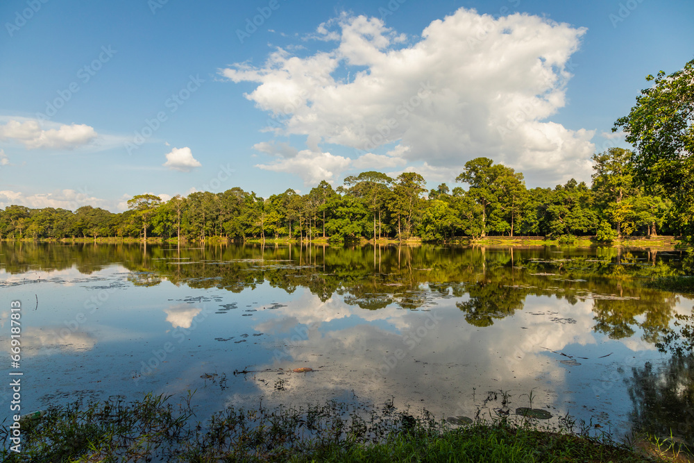 Fototapeta premium Rainforest landscape, reflected above the calm waters of one of the lakes surrounding the ancient city of Angkor, Cambodia