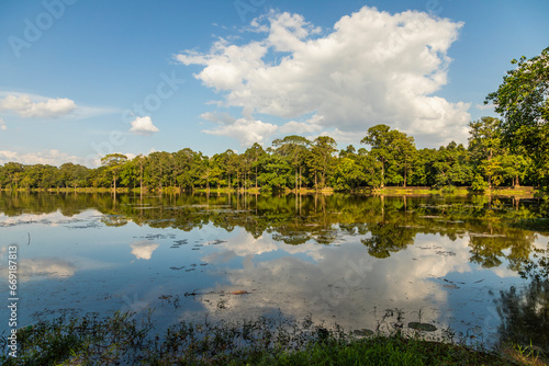 Fototapeta Naklejka Na Ścianę i Meble -  Rainforest landscape, reflected above the calm waters of one of the lakes surrounding the ancient city of Angkor, Cambodia