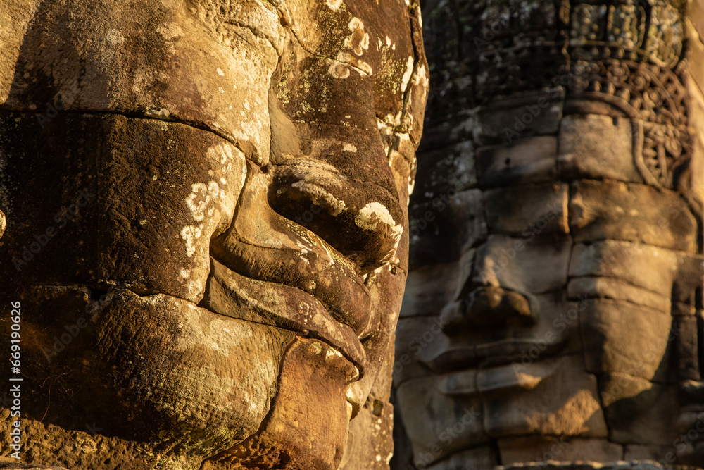 Naklejka premium Two stone faces, sculpted at Bayon temple, illuminated by the last rays of evening sunlight, Angkor, Cambodia.