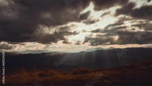 Dark dramatic autumn mountain cloudscape. Epic storm clouds moving fast, rays of rising sun break through the clouds hit the orange meadow. Vintage dark sunset footage time lapse. Nature background