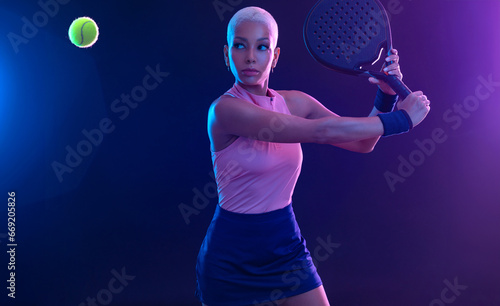 Padel tennis player with racket on tournament. Girl athlete with paddle racket on court with neon colors. Sport concept. Download a high quality photo for design of a sports app or tour events. © Mike Orlov