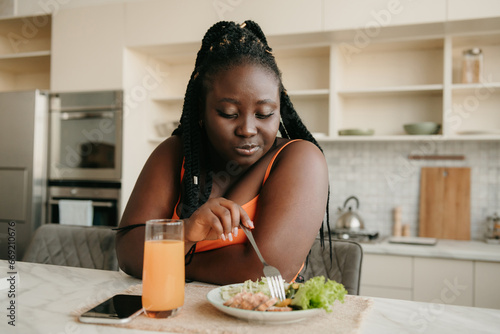 Beautiful plus size African woman enjoying healthy food for lunch at home