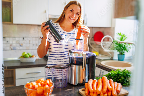 Φωτογραφία A woman making carrot juice from fresh carrots with a home juicer in the kitchen