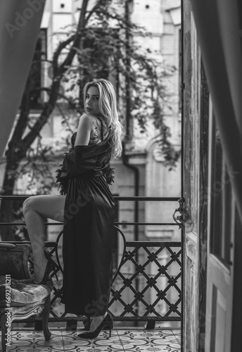 Lady in peignoir with a glass of wine. Sensual photo of European Blonde woman in black silk robe with feathers sleeve. Fashionable concept © T.Den_Team