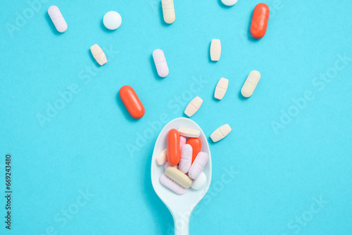Colorful Medicine Pills in White spoon on green tosca background, supplement, vitamin, colorful