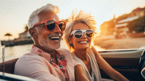 A happy, old husband and wife couple enjoying their retirement - driving a convertible while on a road trip.