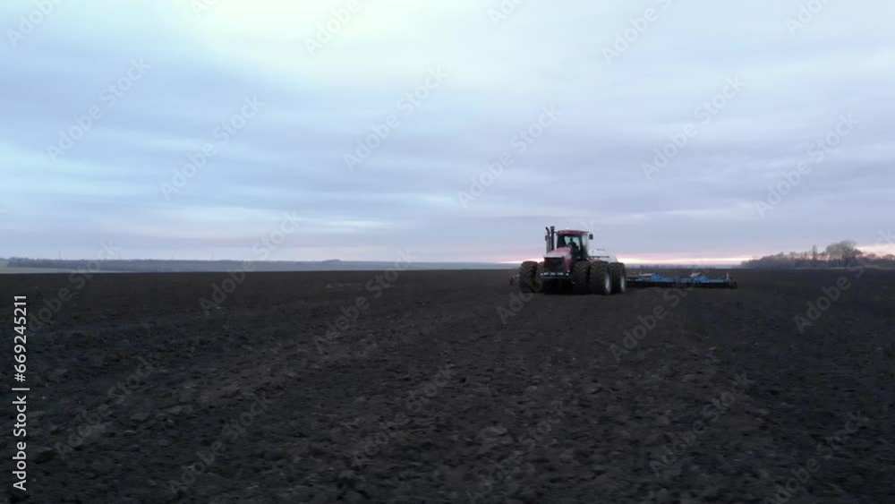 Big red tractor cultivating soil at sunset doing liquid fertilizer injection Big red tractor cultivating soil at sunset doing liquid fertilizer injection
