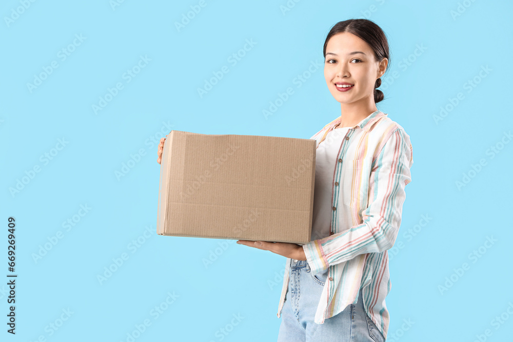 Young Asian woman with parcel on blue background Young Asian woman with parcel on blue background