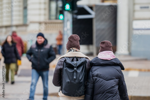 Two girl friends walking along side by side over walkway on green pedestrian traffic light. Wearing autumn warm layerd clothes and bacpack and scarfs photo