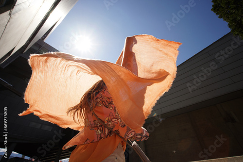 Successful positive woman in orange fashion clothes waving orange scarf in business building environment photo