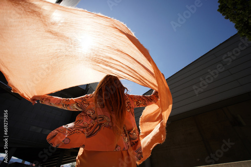 Successful positive woman in orange fashion clothes waving orange scarf in business building environment photo