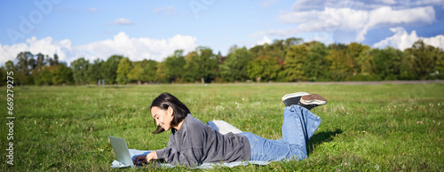Leisure and people. Happy young woman lying in park on blanket, using laptop, relaxing outdoors and watching videos online on computer