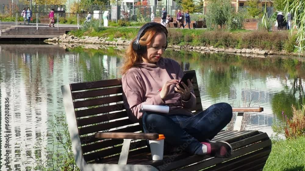 freelancer woman sit on bench in park, uses a smartphone, coffee to go, looks social networks, online training, conference. outdoors rest use laptop pc computer talk by mobile cell phone . People urba