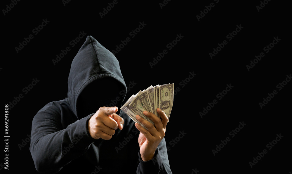 Portrait bandit man hacker one person wearing hood black shirt, sitting onchair and table thief hand holding money payment counting the amount obtained from hijacking or robbing, in dark background - obrazy, fototapety, plakaty 