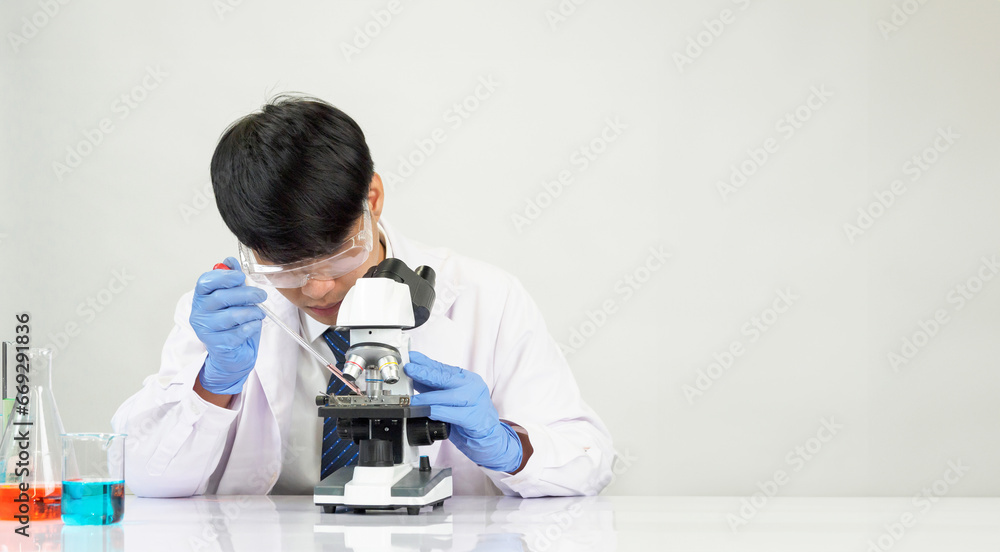 Portrait Asian man student scientist Wearing a doctor gown in the lab looking hand at chemist. caused by mixing reagents in scientific research laboratories with test tubes and microscope on the table Portrait Asian man student scientist Wearing a doctor gown in the lab looking hand at chemist. caused by mixing reagents in scientific research laboratories with test tubes and microscope on the table