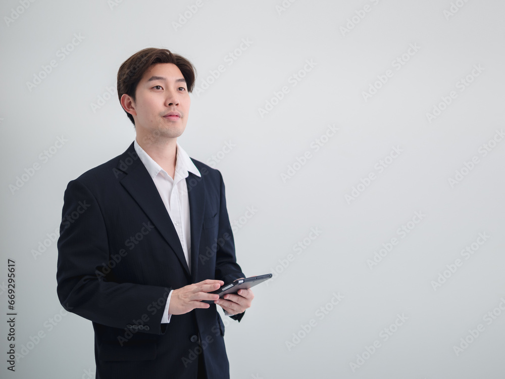 Business man portrait Asian one person wearing a black suit handsome standing looking success committed hand holding mobile phone and laptop ready for work inside the office, with white background Business man portrait Asian one person wearing a black suit handsome standing looking success committed hand holding mobile phone and laptop ready for work inside the office, with white background