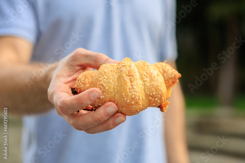 A man s hand holds a croissant  snack and fast food concept. Selective focus on hands with blurred background