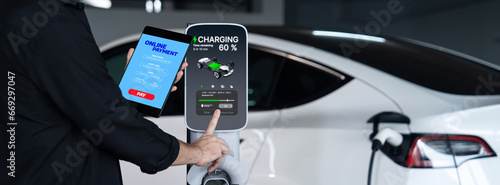 Young man travel with EV electric car to shopping center parking lot charging in downtown city showing urban sustainability lifestyle by green clean rechargeable energy of electric vehicle innards