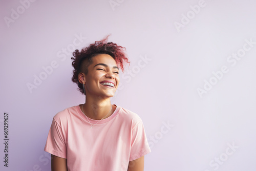 Young laughing gender non-binary person with pink dyed curly hair on a light pink background. Copy space. 