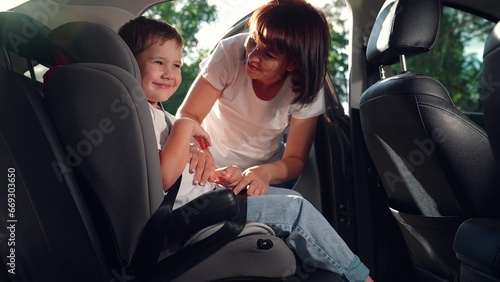 Mom puts her Kid son in car seat, safe car. Happy family. Mother secures her son in car seat using child safety belt. Family road trip. Mom cares about her sons safety. Child sits in car child seat