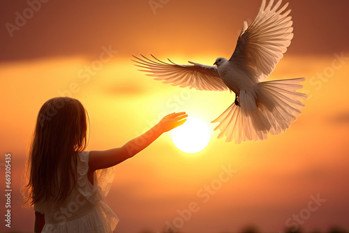 a little girl holding a white bird in her hand as the sun sets behind her and she is looking at it © Golib Tolibov