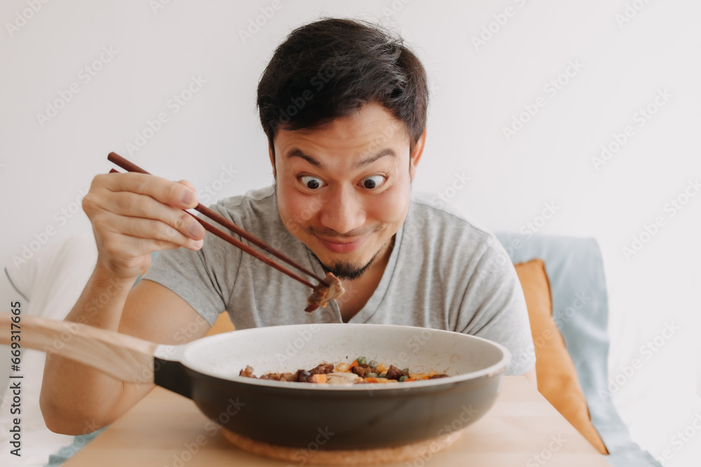 Happy funny face of asian man eating homemade food in the pan with chopsticks. Happy funny face of asian man eating homemade food in the pan with chopsticks.