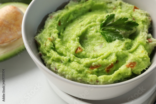 Bowl of delicious guacamole with parsley on white table, closeup