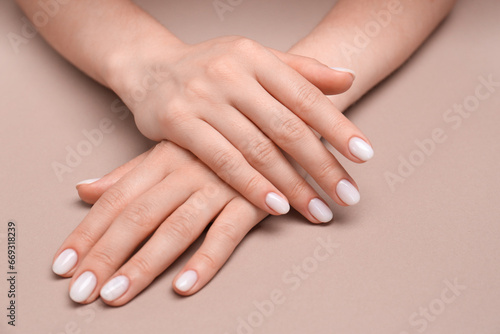 Woman showing her manicured hands with white nail polish on light brown background  closeup