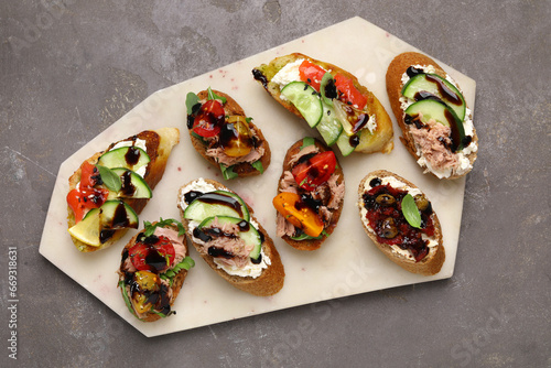 Delicious bruschettas with balsamic vinegar and different toppings on grey textured table, top view
