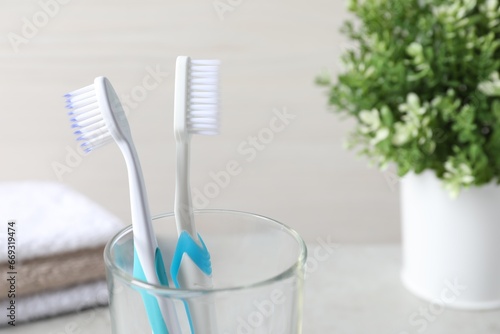 Plastic toothbrushes in glass holder against light background  closeup