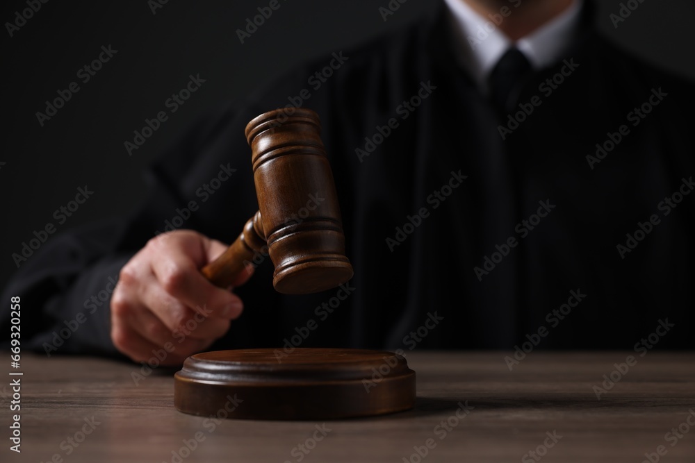 Judge with gavel sitting at wooden table against black background, closeup Judge with gavel sitting at wooden table against black background, closeup
