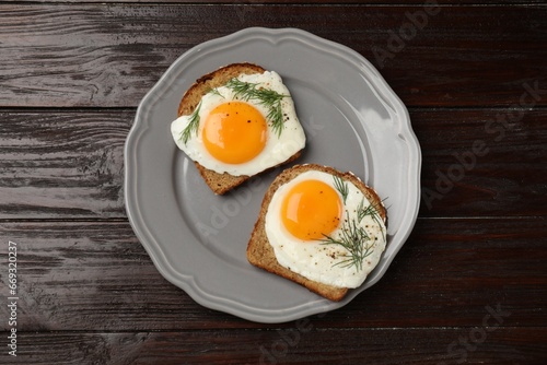 Plate with tasty fried eggs, slices of bread and dill on dark wooden table, top view
