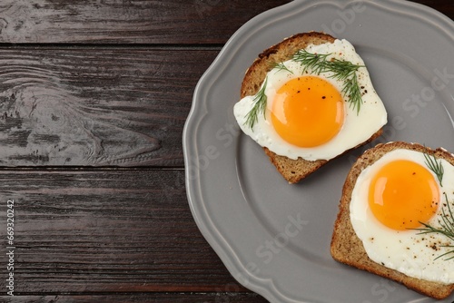 Plate with tasty fried eggs, slices of bread and dill on dark wooden table, top view. Space for text