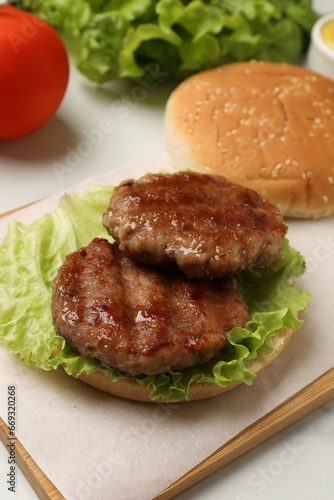 Delicious fried patties, lettuce and bun on white table. Making hamburger