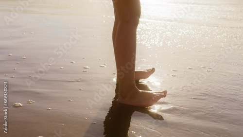 Close up view of barefoot kid runs on ocean waves and jump in water. Cute little girl having fun at sunset. Adorable baby kid with long blonde hair in flower dress enjoying nature at ocean beach 4K