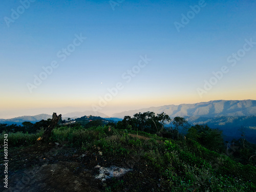The small moon at the sky over the mountain at the sunrise time with the ash on the ground at the foreground